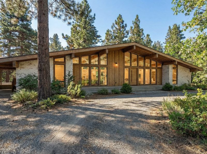 Front elevation of the 2136 house among the pines, with wood siding and a gravel drive